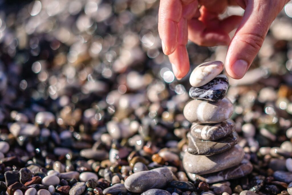pexels-photo-12956093 A hand carefully stacks smooth stones outdoors, symbolizing balance and tranquility.